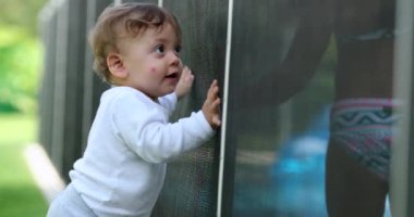 Yüzme havuzu çitlerinin yanında duran sevimli bebek. Çocukla etkileşim halinde olan çocuk