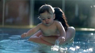 Mother kissing and holding baby infant at the swimming pool water