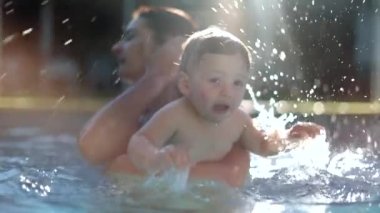 Happy baby infant at the swimming pool splashing water with mother