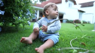 Dışarıda yeni yürümeye başlayan bebek. Ev bahçesinde bir bebek dalla oynuyor.