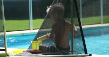 Yaz tatili boyunca havuzda oyuncaklarla oynayan samimi bir çocuk.