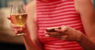 Akıllı telefonuyla gülen kadın bira içiyor.