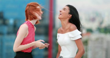 Cep telefonu ekranına bakan iki genç kadın kahkahalara boğuldu. Gerçek hayat spontane kahkaha ve gülümseme