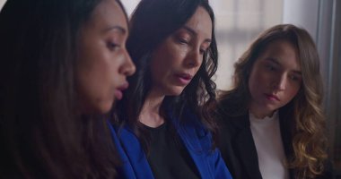 Kadın çalışanlara grafikler ve belgeler gösteren bir iş kadını. Ofis işyerinde iş tartışan bir grup insan. Çalışanlar işten bahsediyor.