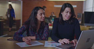 Geceleri bilgisayarın önünde çalışan iki farklı kadın çalışan ofis masasında oturup iş hakkında konuşuyorlar. Genç kadınlar akşamları modern işyerlerinde çalışırlar.