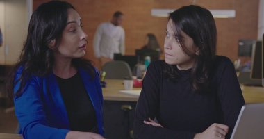 Geceleri ofiste çalışan iki kadın çalışan. Modern iş yeri kurumsal hayatı. Yaşlı iş kadını yöneticisi, çalışmalarını genç çalışanlara grafik ve belge göstererek anlatıyor