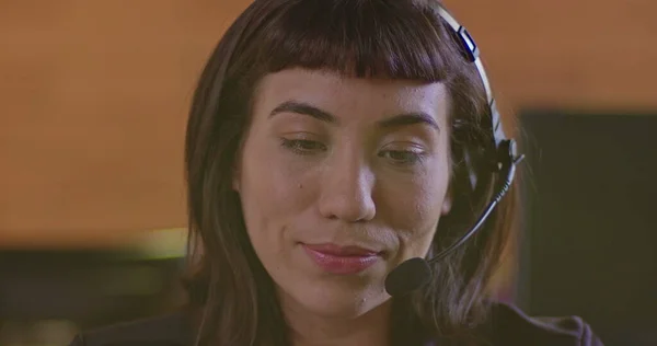 Portrait of a happy hispanic woman wearing headset speaking with customer online in front of computer screen. Female employee at call center support speaking with person