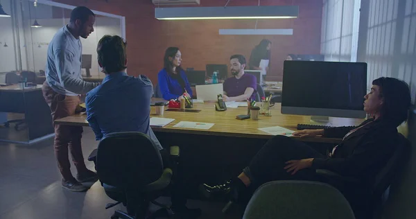 Group of people working inside corporate office at night. Young men and women employees in front of computers. Workspace and businesspeople concept. Millennials staff at work