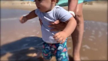Sahilde ilk kez yürümeye başlayan bir çocuk. Bebek suyu hissediyor.