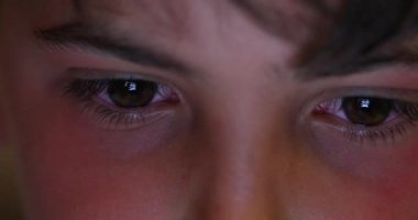 Macro eyes of young boy staring at screen at night. Child looking at tech device