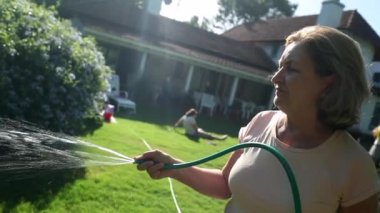 Senior woman in 70s watering plants and garden in backyard home during sunny beautiful day