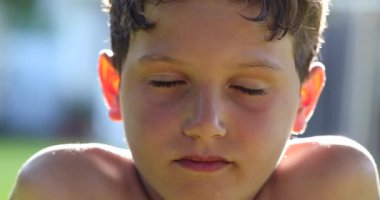 Handsome child boy face portrait smiling to camera outside in sunlight. Kid closing and opening eyes feeling happy and smiling