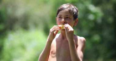 Portrait of child boy eating healthy corn cob outside after pool