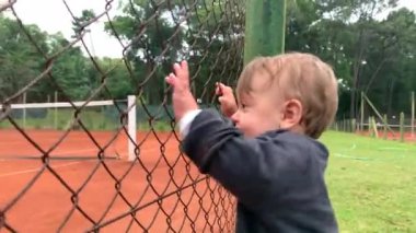 Baby infant holding into tennis fence watching game