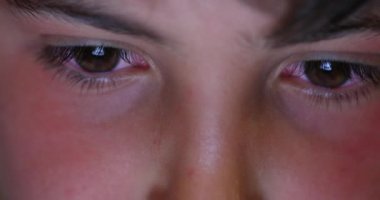 Kid eyes staring at screen light at night. Boy addicted to electronic watching phone or tablet device
