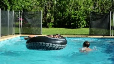 Güneşli bir günde çocuklar havuzda oynuyorlar. Şişme yataktaki çocuk