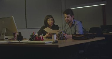 Geceleri ofiste mesai yapan iki kişi. Erkek ve bayan çalışanlar gece geç saatlerde işyerinde oturmuş evrak ve evrak işlerini gözden geçiriyorlar.