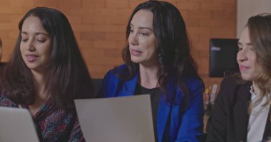 İş yerindeki kadınlar dizüstü bilgisayarın önünde iş konuşuyorlar. Kadın lider, genç bayan personele koçluk yapıyor. Geceleri ofiste işbirliği yapan insanlar.