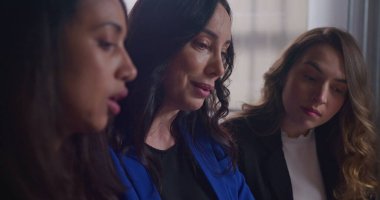 Kadın çalışanlara grafikler ve belgeler gösteren bir iş kadını. Ofis işyerinde iş tartışan bir grup insan. Çalışanlar işten bahsediyor.
