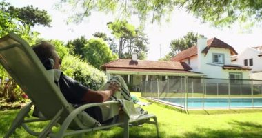 Senior man resting by pool lying down and relaxing in backyard home