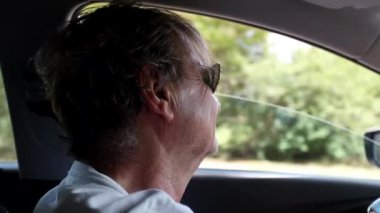 Happy senior man driving on road wearing sunglasses. Relaxed older man driver on countryroad