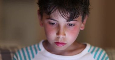 Boys in front of tablet screen with blue light glowing on face at night. Children watching content online browsing internet