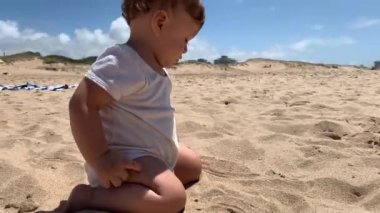 Kumsaldaki bebek ağzına kum koyuyor.