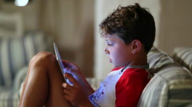 Gizli çocuk, gece yatmadan önce tablet kullanıyor. Kanepedeki genç çocuk internette oyun oynuyor.