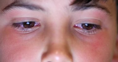 Macro close-up of young boy face eyes detail staring at tablet device screen watching content online