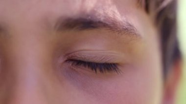 Çocuk gözlerini açıyor ve kapıyor, çocuk dışarıdaki makro gözlere gözlerini kısıyor. Çocuk kameraya çok yakından bakıyor.
