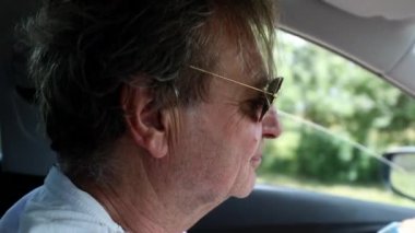 Senior man driving on countryroad. Relaxed happy older man in 70s wearing sunglasses and driving on road