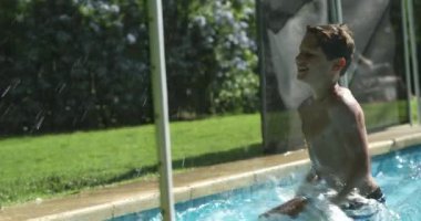 Havuz suyundaki çocuk havuzun dışına su sıçratıyor. Çocuk eliyle su sıçratıyor.