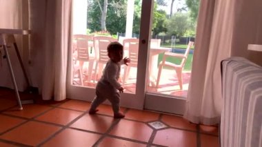 Baby infant learning to stand at home leaning on window looking outside