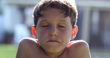 Male kid face portrait with eyes closed. Handsome child in sunlight outside opening eye