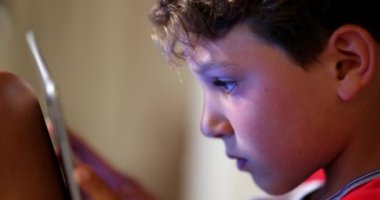 Digital native child addicted to tablet device. Young boy absorbed by screen playing video-game in competition