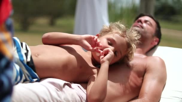 一家人都在享受暑假 父亲休息和日光浴 孩子蹒跚学步躺在爸爸胸前 — 图库视频影像