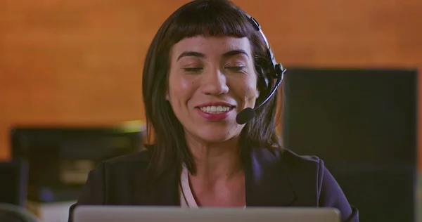 Portrait of a happy hispanic woman wearing headset speaking with customer online in front of computer screen. Female employee at call center support speaking with person