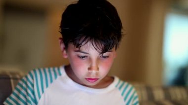 Yüzünde ışık parlayan tablet ekrana bakan genç bir çocuk. Geceleri teknoloji kullanan çocuk