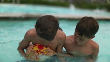 Yaz günü açık havada yüzme havuzunda el topu oynayan kardeşler. Çocuklar suyun içinde top için savaşıyor ve yarışıyorlar.