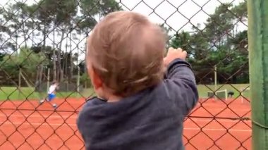 Baby infant holding into tennis fence watching game