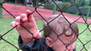 Cute baby holding into game fence watching from the outside