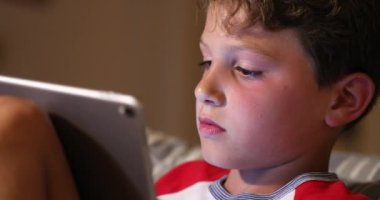 Geceleri tablet kullanan küçük bir çocuk. Teknolojiye bağlı çocuk nesli yarışmada gece bilgisayar oyunu oynuyor.