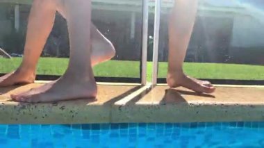 Çocuklar yaz günü havuzda oynuyorlar, çocuk arkadaşını suya atıyor.