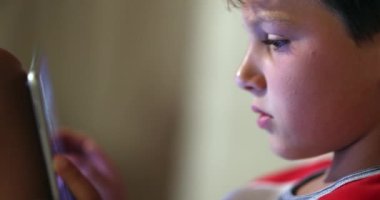 Kid using tablet screen at night. Digital native young boy browsing internet online watching content