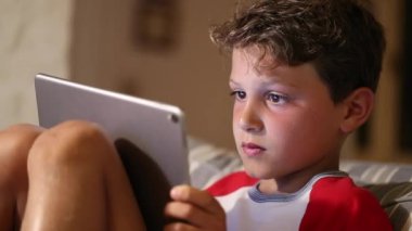 Çocuk evde tablet tutarken mutlu bir tepki veriyor.