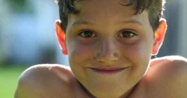 Handsome young boy child face smiling feeling happy and joy in outdoor sunlight. Kid portrait real life smile