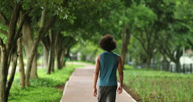 Back of african man walking at green park path surrounded by nature, contemplating life