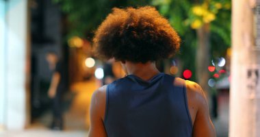 Back of african american black man walking in city sidewalk at night during drizzle