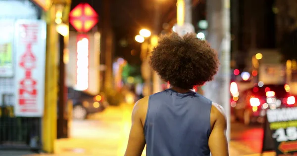 Back Young black african man walking in city at night when raining, downtown