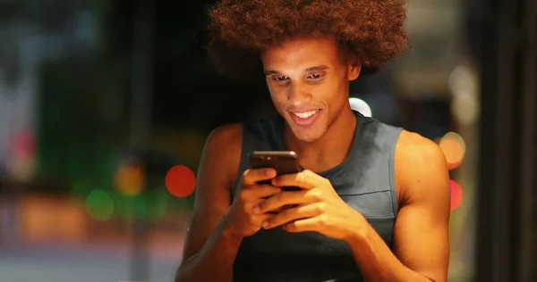 Casual candid african man staring at smartphone in city typing at night